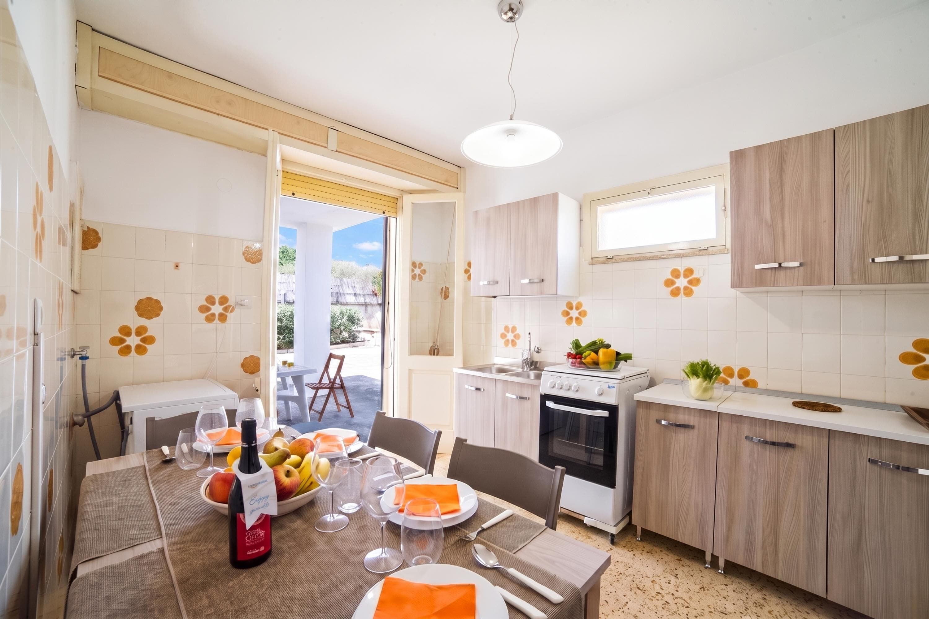 A modern kitchen with white cabinets, a dining area with a table set for two, and a view of the outdoors.