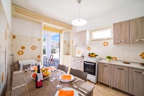 A modern kitchen with white cabinets, a dining area with a table set for two, and a view of the outdoors. - Giulia Sea View Villas (Santa Cesarea Terme)