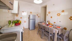 A modern kitchen with a dining area, equipped with a refrigerator, a sink, and a table set for two with plates, cutlery, and a bowl of fruit. - Giulia Sea View Villas (Santa Cesarea Terme)