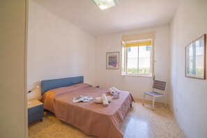 Une chambre avec un lit simple, une chaise, une table de chevet, une fenêtre donnant sur un paysage agréable et un tableau encadré au mur.