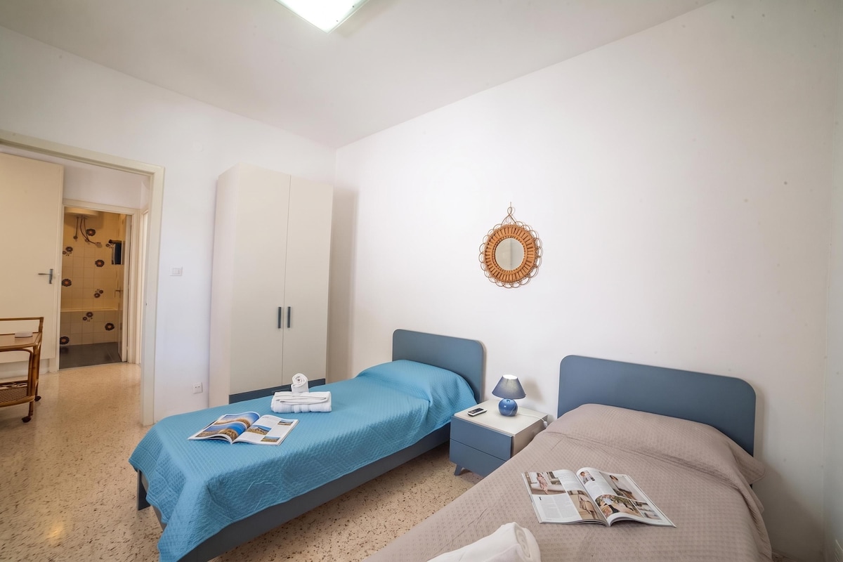Quarto com duas camas, um guarda-roupa, um espelho e uma pequena mesa com abajur.