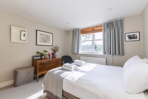 A bedroom with a bed, a dresser, a chair, a radiator, and framed pictures on the wall.