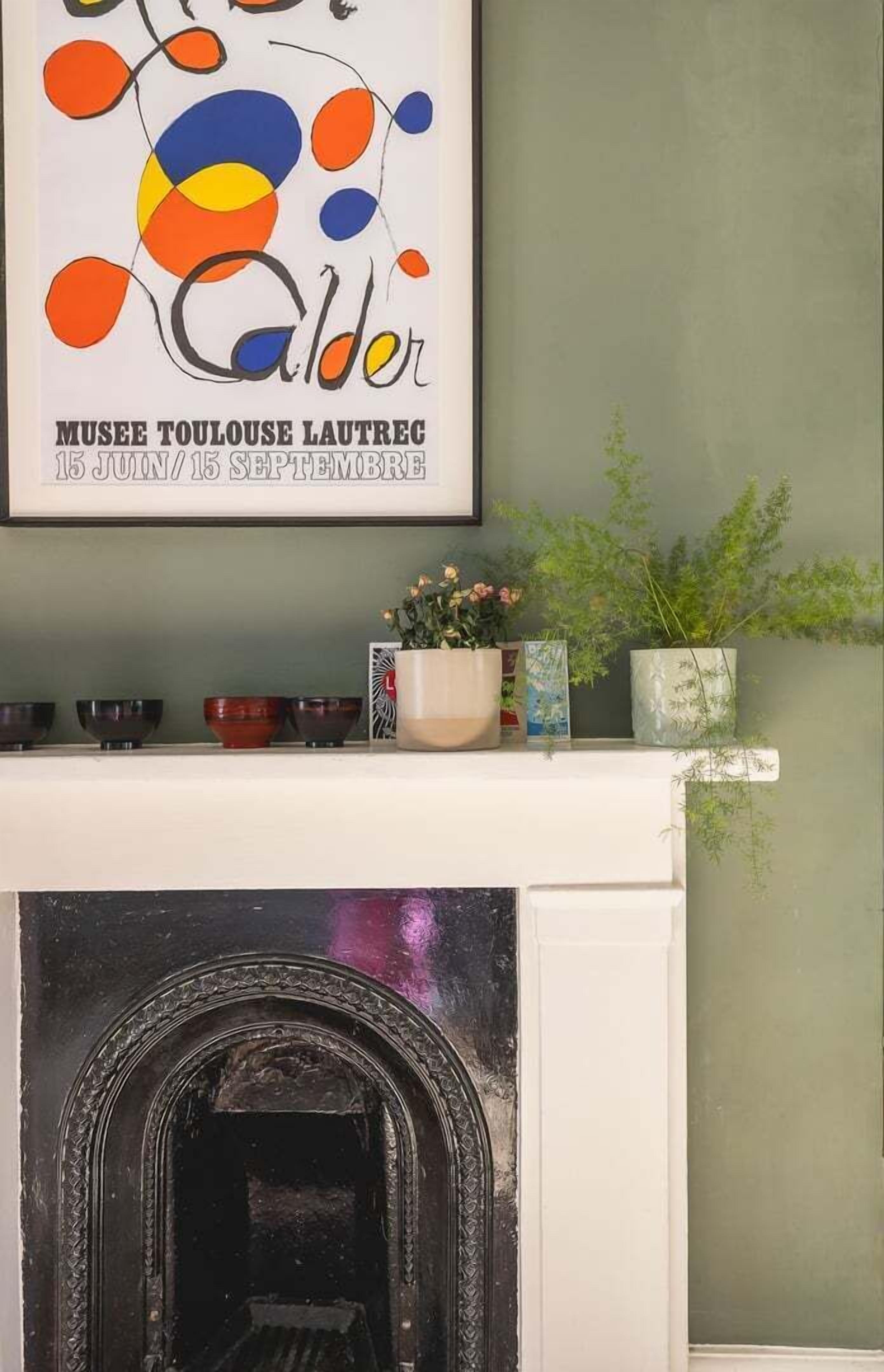 Un caminetto con un quadro astratto incorniciato sopra, una mensola con oggetti decorativi e una parete verde.