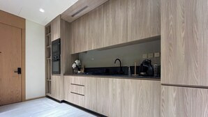 A modern kitchen with wood cabinetry, a black countertop, and stainless steel appliances. - Stylish 1BR Penthouse in The Autograph  (Dubai)