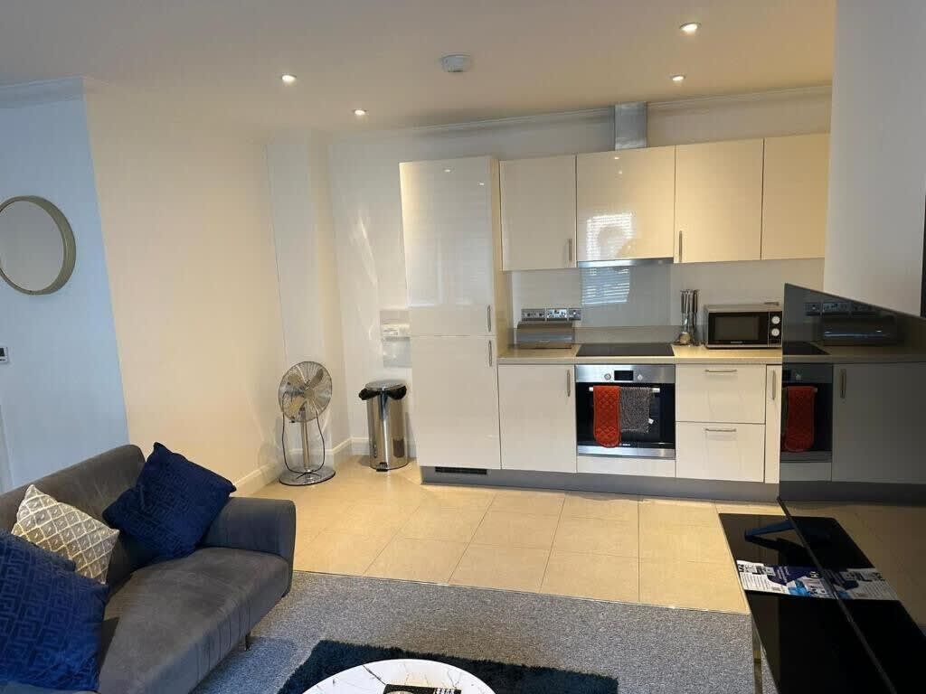 A modern kitchen with white cabinets, a microwave, oven, and a dishwasher. There is a grey sofa with blue cushions in the living area.
