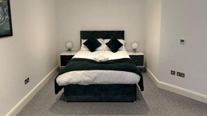 A modern bedroom with a large bed, two bedside tables, and a headboard. - DH Aparthotels - Cromwell Apartment (Huntingdon)