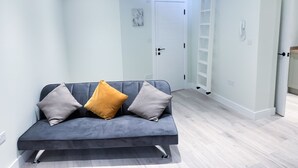 Una sala de estar moderna con un sofá gris, dos cojines, una escalera de madera y una puerta blanca.