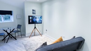 Una sala moderna con una mesa de vidrio, dos sillones, un sofá y un televisor de pantalla plana grande montado sobre un trípode.