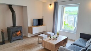 Ein modernes Wohnzimmer mit Kaminofen, Flachbildfernseher in einer Wandnische, grauem Sofa und Couchtisch aus Holz.