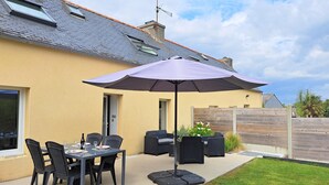 Eine Terrasse im Freien mit Tisch, Stühlen und einem lila Sonnenschirm, darüber hinaus eine Rasenfläche.