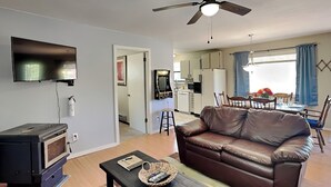 A living room with a leather sofa, a coffee table with a basket, a TV, and a fireplace. - Knotty Pines Cabin | Pet-Friendly, Great Location (Ruidoso)