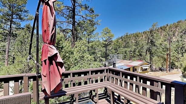 A wooden deck with a pool, surrounded by trees and a small building in the background. - Knotty Pines Cabin | Pet-Friendly, Great Location (Ruidoso)