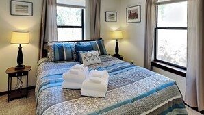 A neatly arranged hotel room with a large bed, two bedside lamps, and a view of a snowy landscape through the windows. - Knotty Pines Cabin | Pet-Friendly, Great Location (Ruidoso)