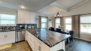 A modern kitchen with white cabinets, a black marble countertop, and a stainless steel dishwasher.