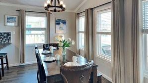 A dining area with a wooden table set for four, a vase with white flowers, and a painting on the wall.