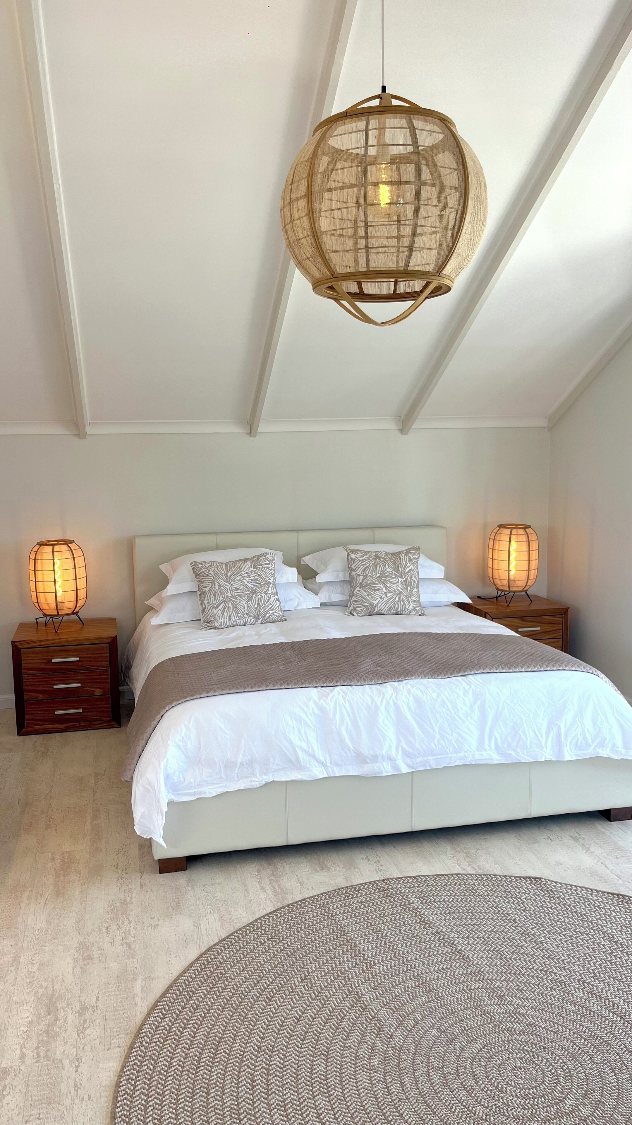 Ein Schlafzimmer mit einem großen Bett, zwei Nachttischen mit Lampen, einer gewebten Deckenleuchte und einem strukturierten Teppich.
