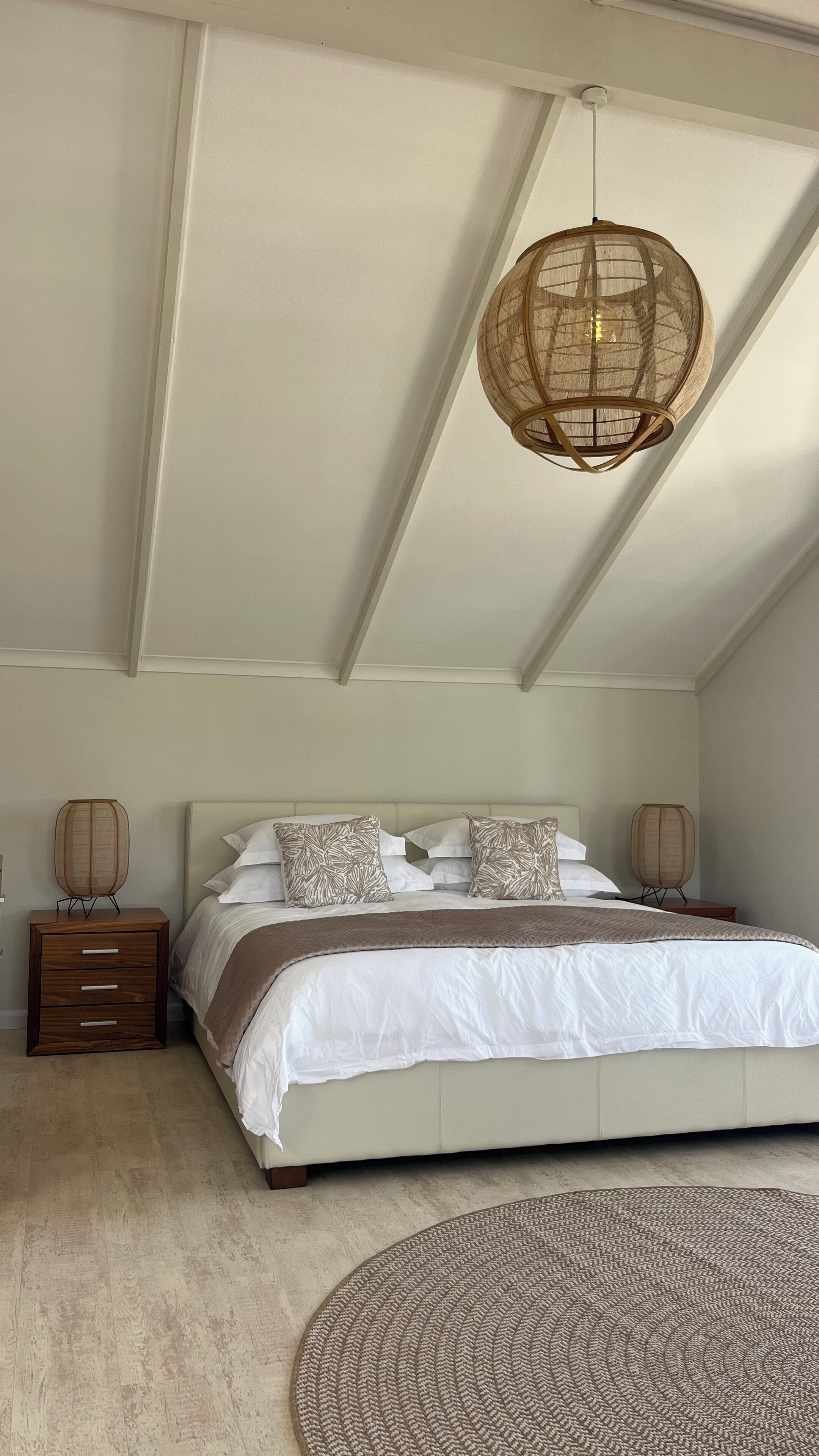 Ein Schlafzimmer mit einem großen Bett, zwei Nachttischen, einer Hängeleuchte und einem runden Teppich.