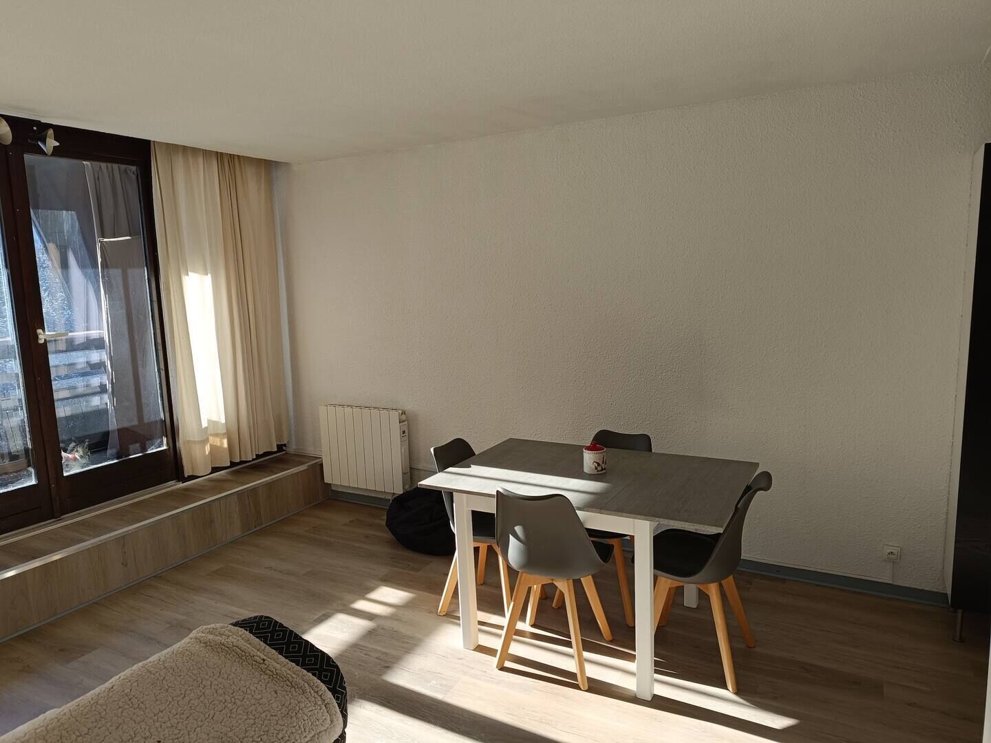 Una sala de estar moderna con una mesa de comedor, cuatro sillas, un sofá, un radiador y un ventanal con cortinas.