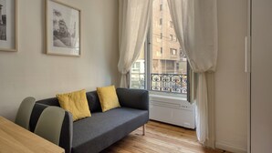 A modern living room with a grey sofa, two yellow cushions, a wooden table, and a window with white curtains. - Classy apartment near Duomo di Milano (Milan)