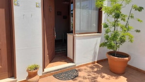 A residential entrance with a wooden door, a potted plant, and a window with a view. - Turismo Rurale Al Benefizio  (Monforte San Giorgio)