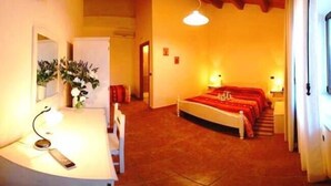Una habitación de hotel con una cama, mesitas de noche, un escritorio con silla, televisor y espejo.