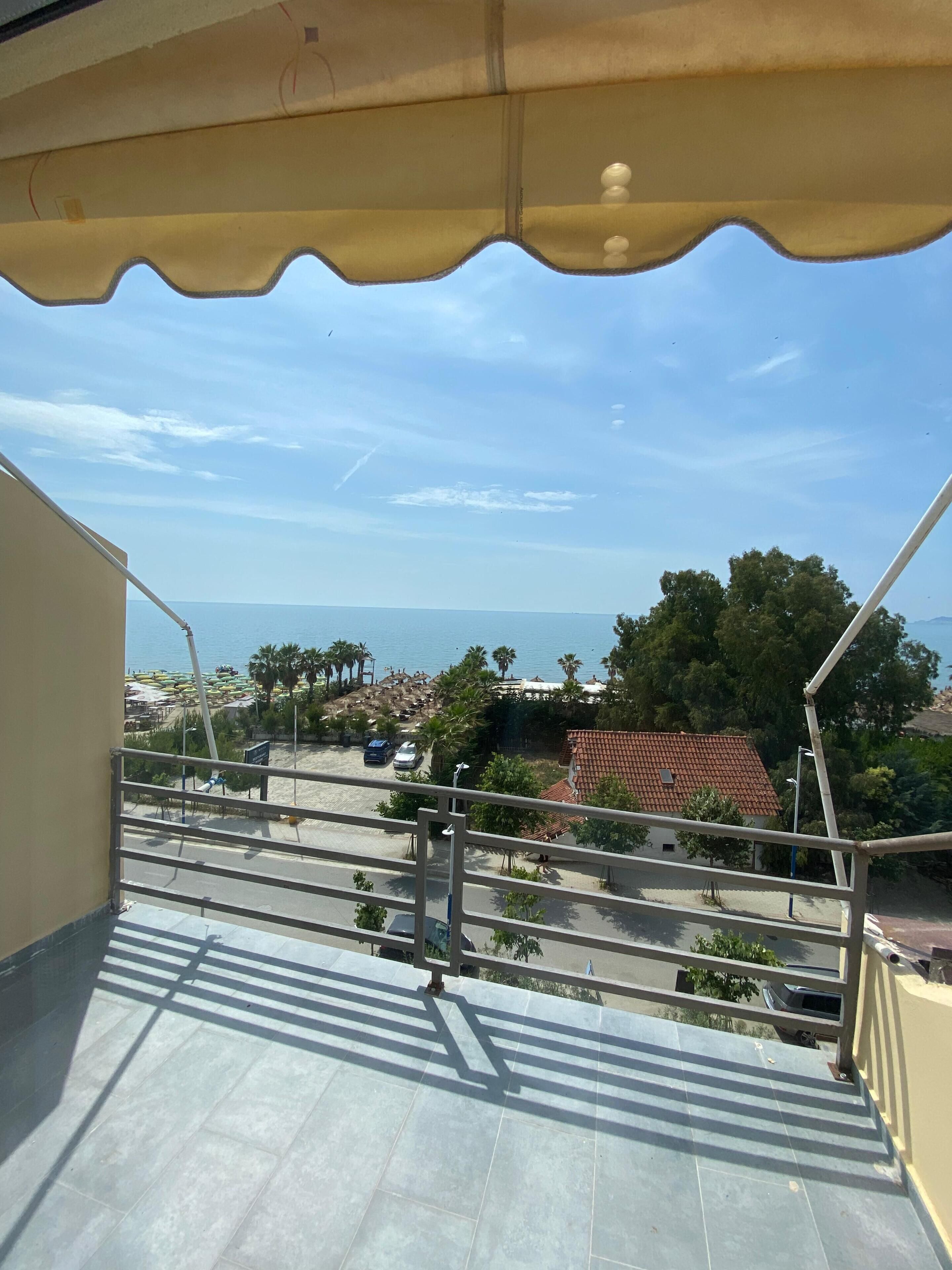 Un balcon avec vue sur la plage, un espace de stationnement et un bâtiment doté d’un toit en tuiles.