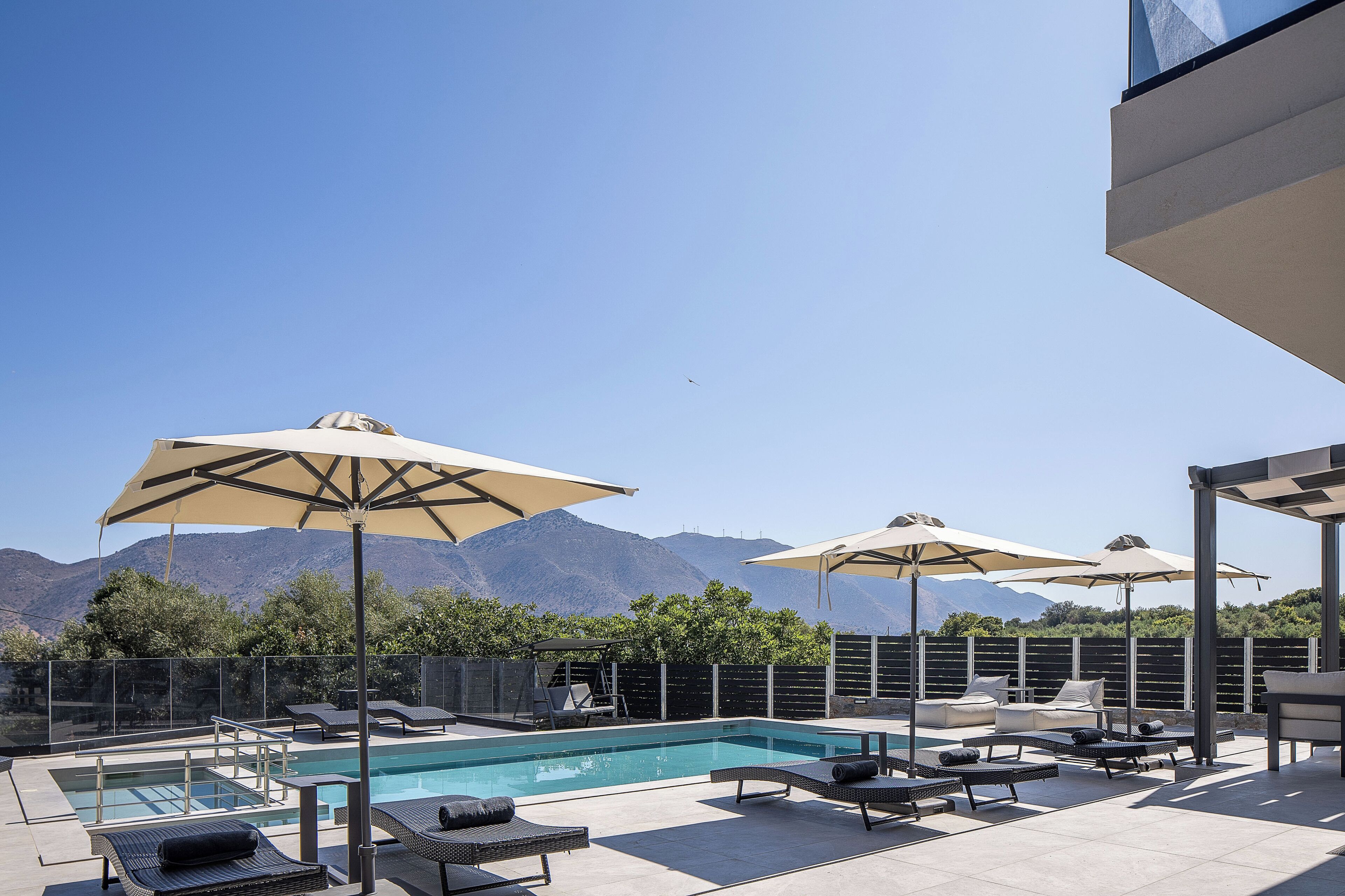 A rooftop pool area with lounge chairs and umbrellas, a swimming pool, and a mountain view.