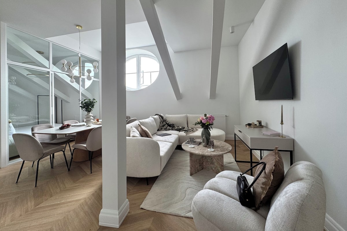 A modern living room with a dining area, a sofa set, a coffee table, and a TV mounted on the wall.