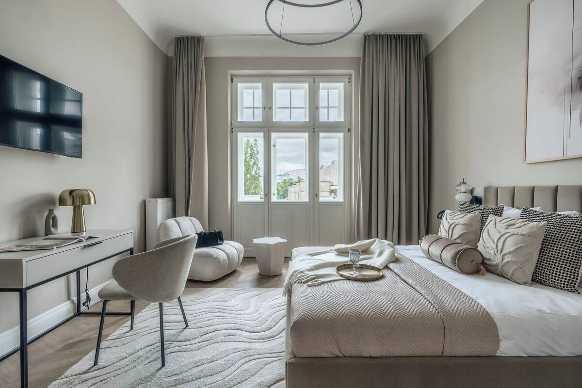 A modern bedroom with a large bed, a desk, a chair, and a TV.