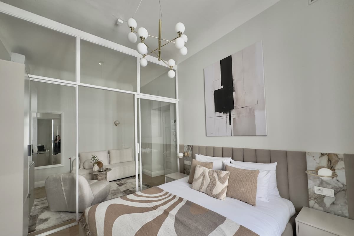 A modern bedroom with a large bed, a walk-in closet, and a contemporary chandelier.