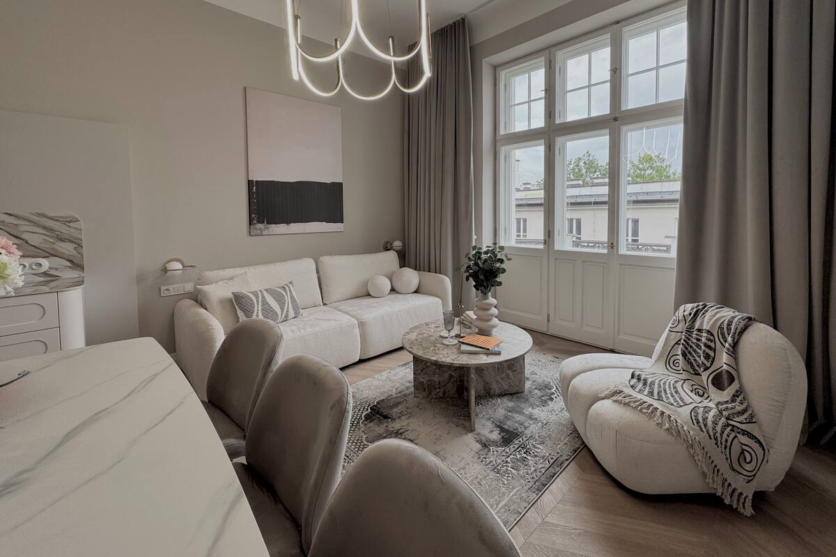 A modern living room with a sofa, armchairs, a coffee table, and a chandelier.