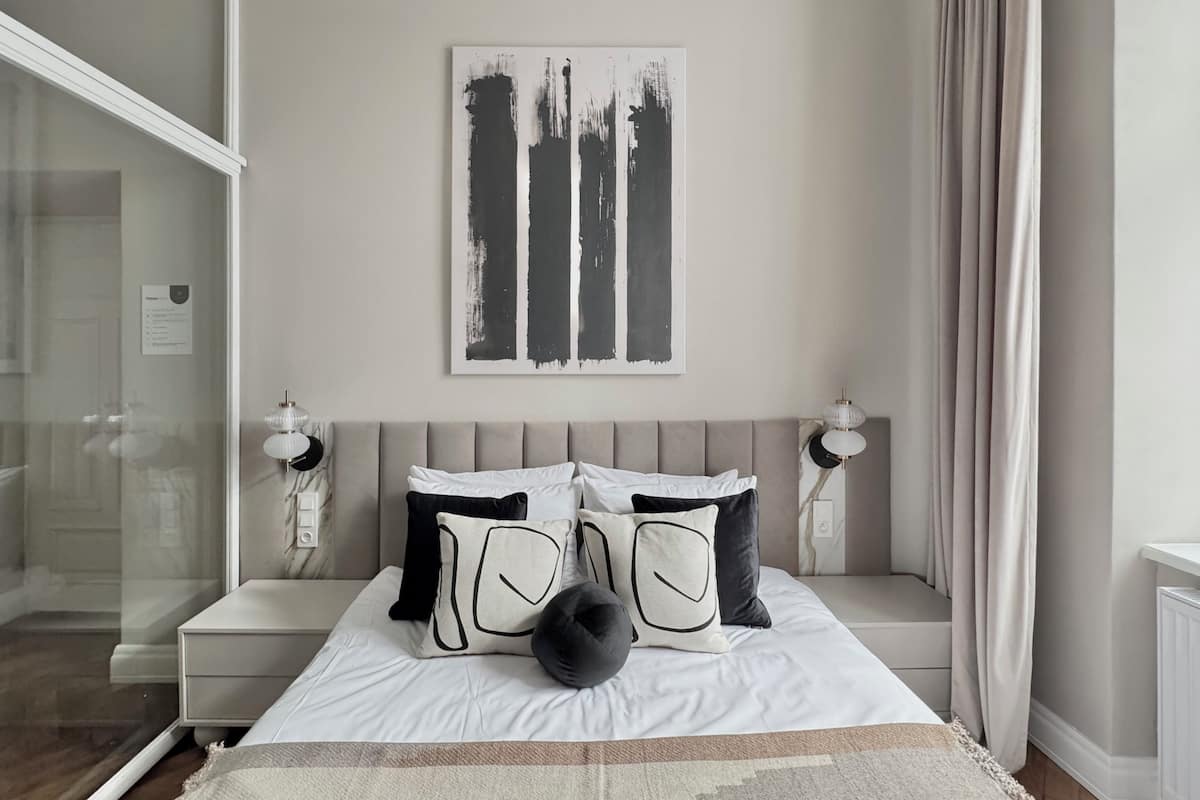 A bedroom with a bed, bedside tables, a wall-mounted artwork, and a window with curtains.