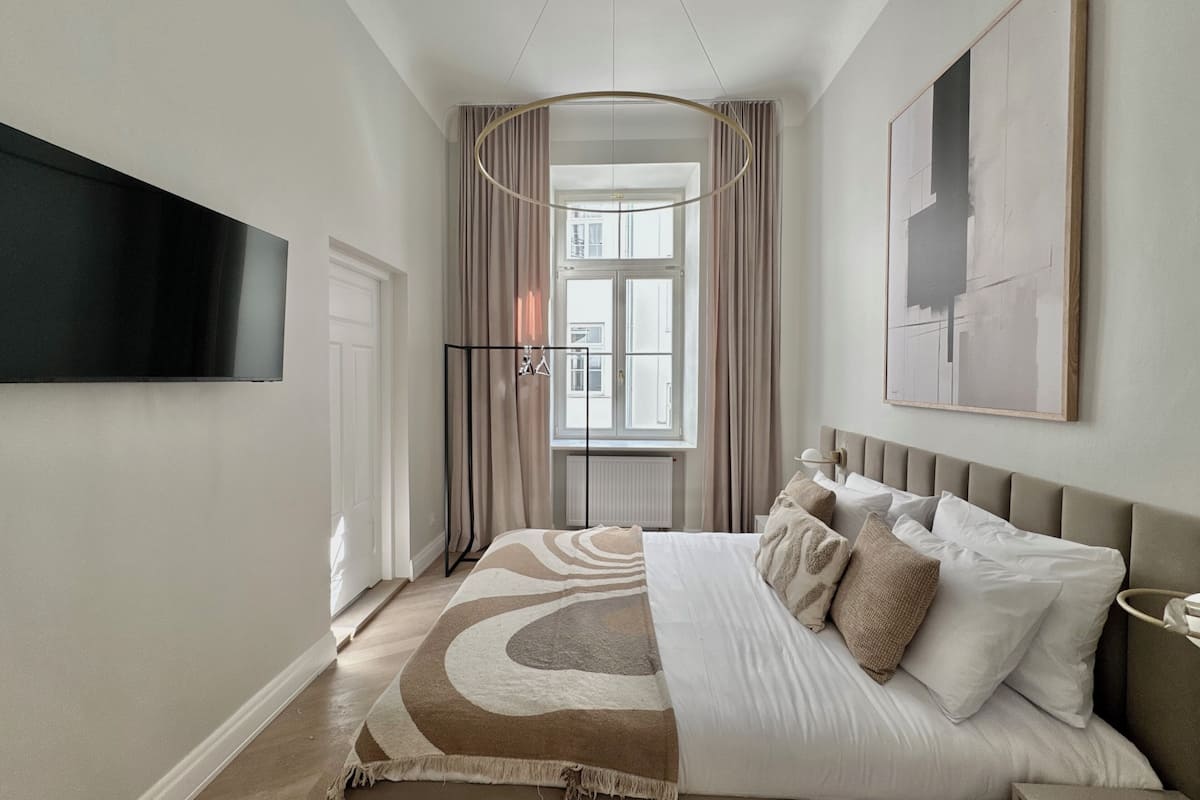 A modern hotel room with a large bed, a flat-screen TV, a window with curtains, and a painting on the wall.