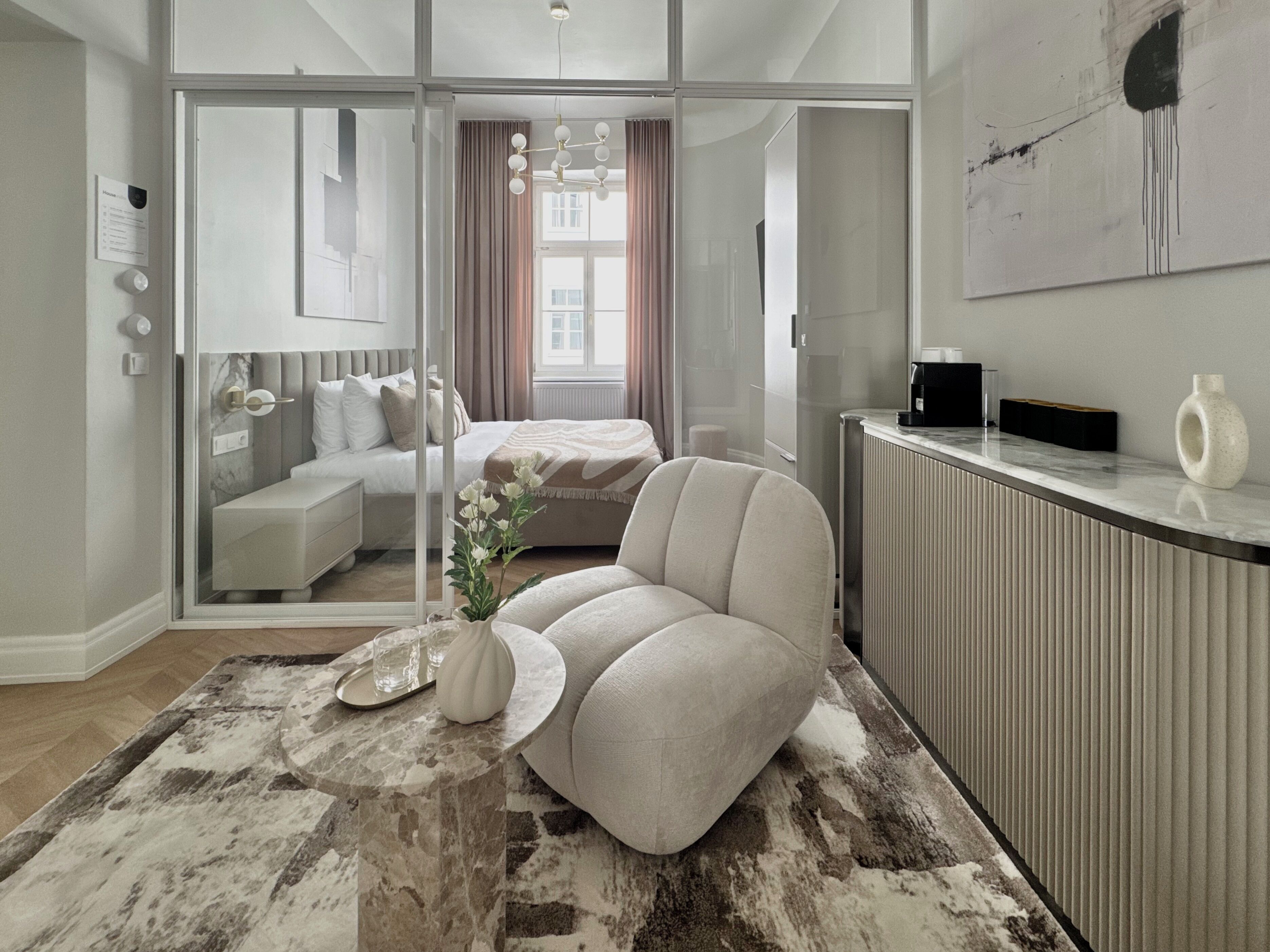Ein modernes Schlafzimmer mit Glastür zum Badezimmer, einem Sofa, einer Kaffeemaschine und einem Heizkörper.