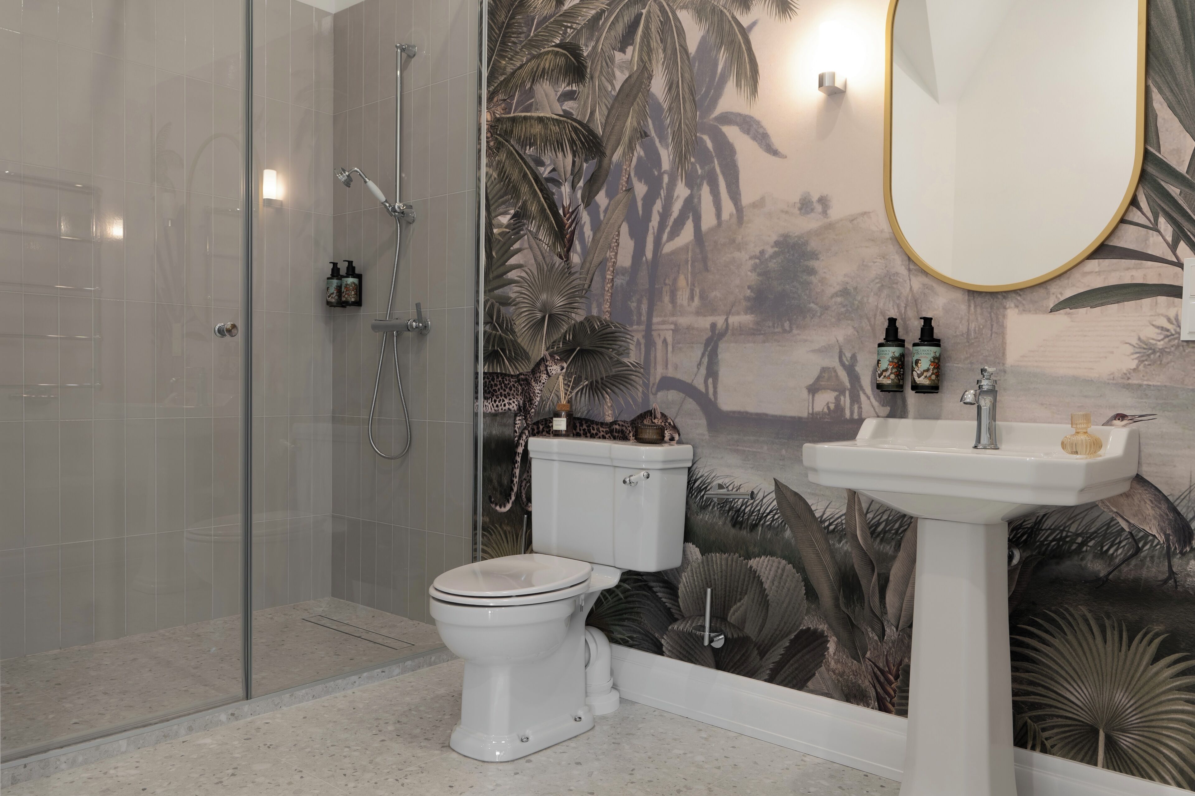 A bathroom with a glass shower enclosure, a toilet, a sink with a mirror, and a decorative wall mural.