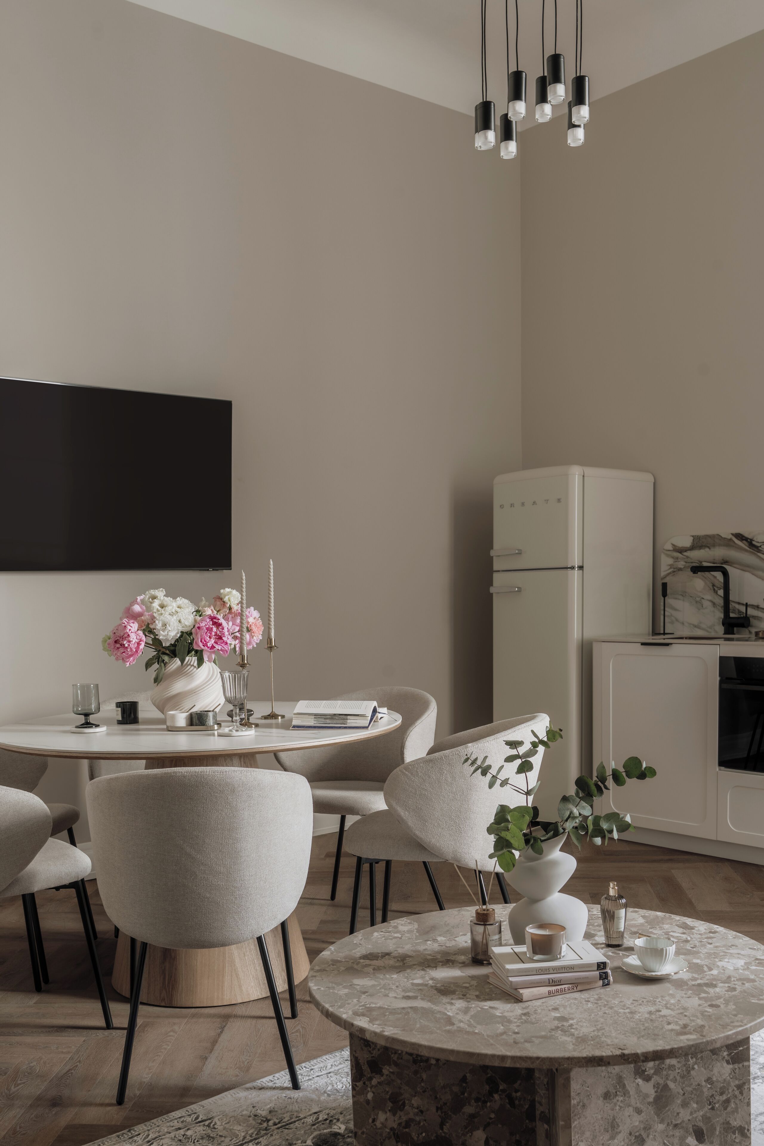 A modern living room with a round marble coffee table, a white sofa, and a dining area with a white refrigerator.