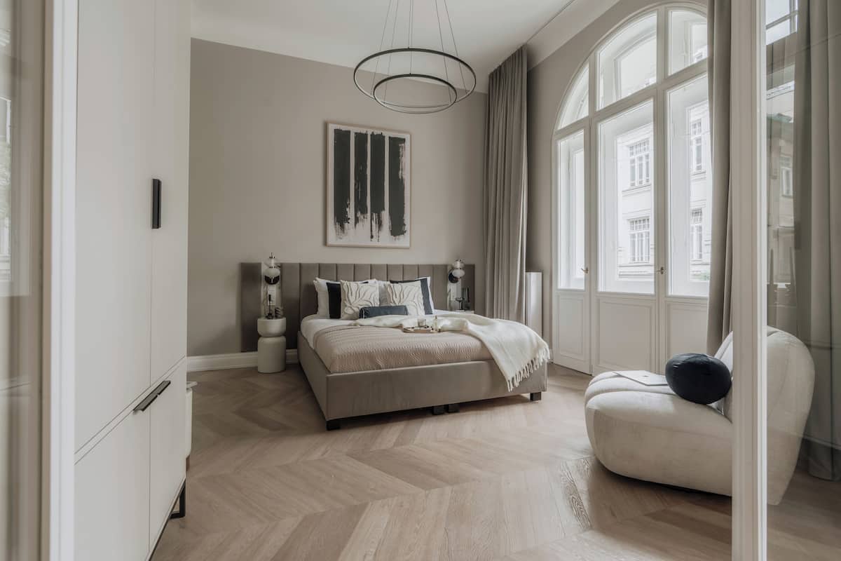 A modern bedroom with a large bed, a bedside table, a chair, and a window with curtains.