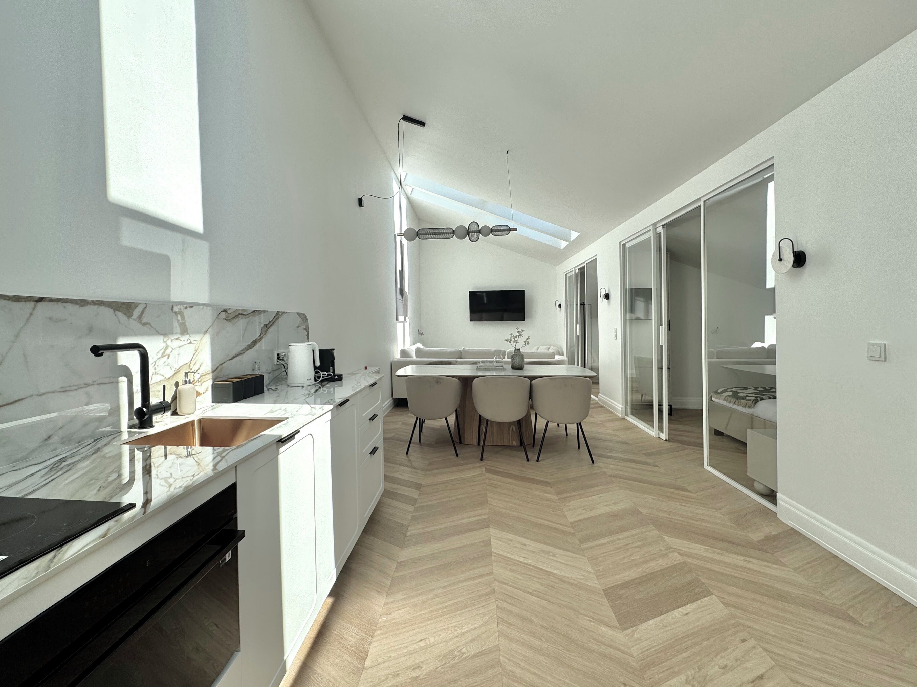A modern kitchen with a marble countertop, a built-in oven, and a dining area with a table and chairs.