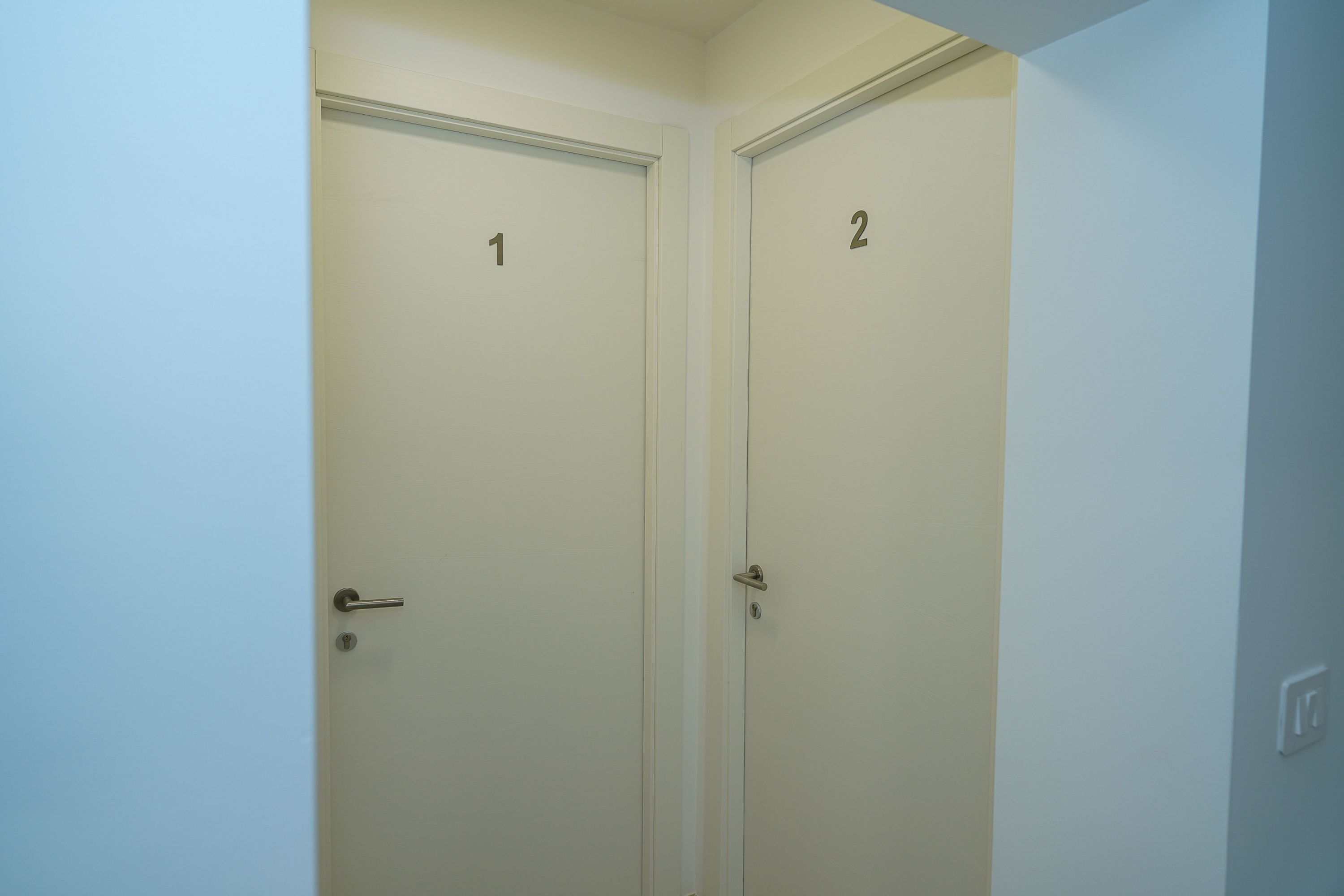 Dos puertas cerradas, con los números 1 y 2, en un pasillo de paredes blancas.