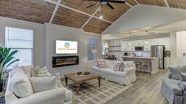 A spacious living room with a fireplace, white sofas, a coffee table, and a kitchen area with modern appliances.