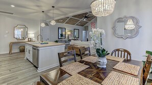A modern kitchen with a central island, wooden dining table, and a chandelier.