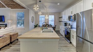 A modern kitchen with a central island, stainless steel appliances, pendant lighting, and a dining area with a view.
