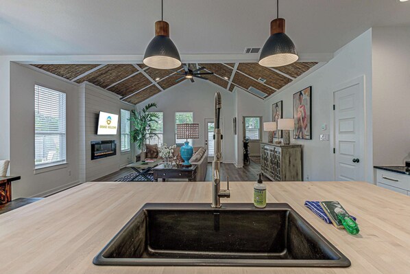 A kitchen with a large sink, wooden ceiling, and pendant lighting.