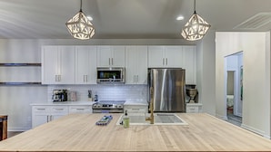 A modern kitchen with white cabinets, stainless steel appliances, and a wooden island. - 6BD Retreat for 14 Fire Pit | Patio | Lake Access (Cottonwood Shores)