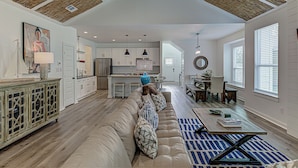 A spacious living area with a high ceiling, a large sofa, a dining table, and a kitchen in the background. - 6BD Retreat for 14 Fire Pit | Patio | Lake Access (Cottonwood Shores)