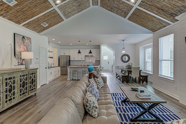 A spacious living area with a high ceiling, a large sofa, a dining table, and a kitchen in the background.