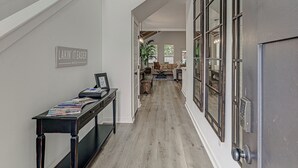 A hallway with a staircase, a table with magazines, a sign reading 'LAKIN' IT EASIER,' and a door with a keypad lock. - 6BD Retreat for 14 Fire Pit | Patio | Lake Access (Cottonwood Shores)