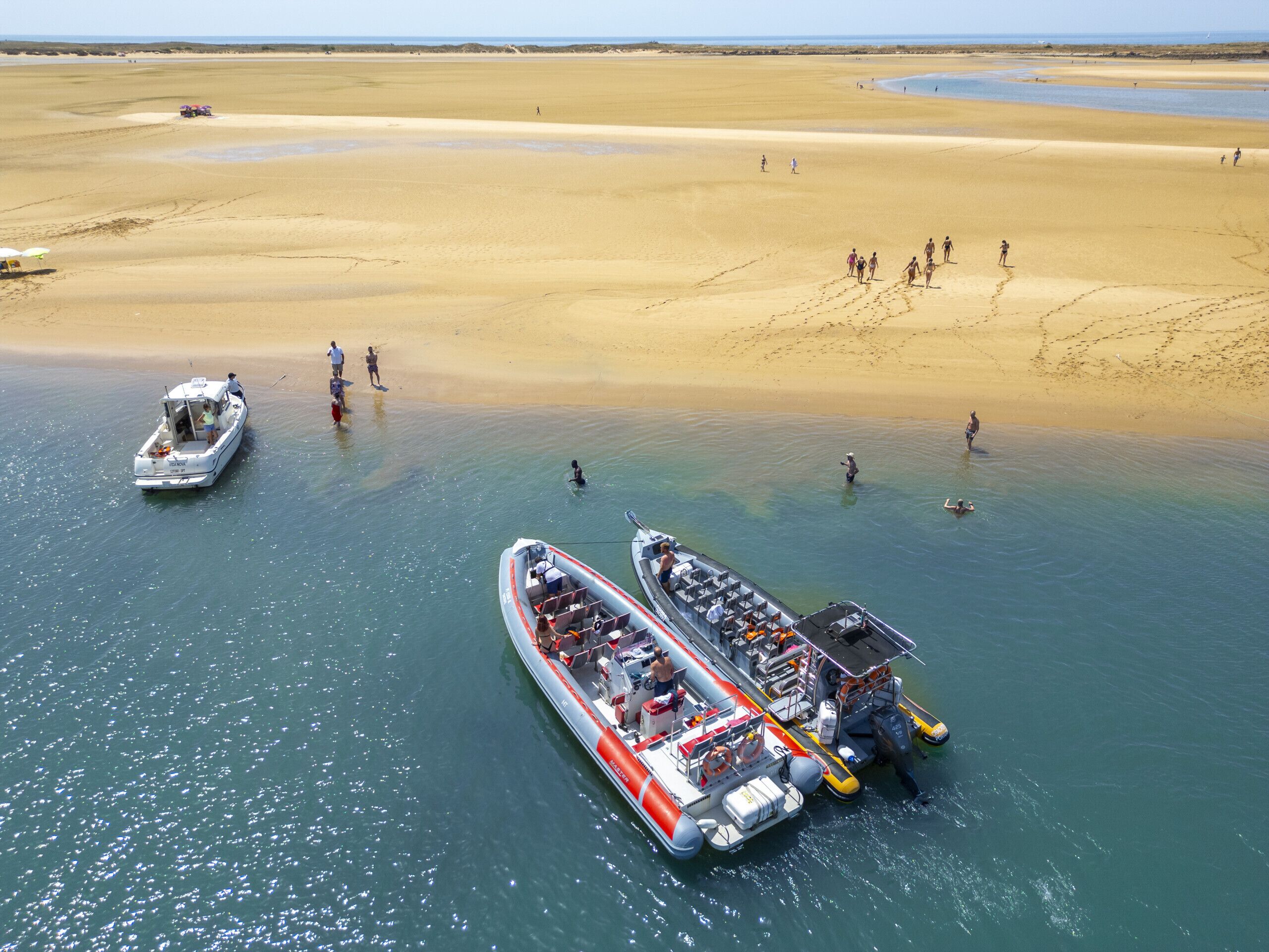 Ein großes Boot liegt an einem Strand mit sandigem Ufer, Menschen laufen am Strand entlang.