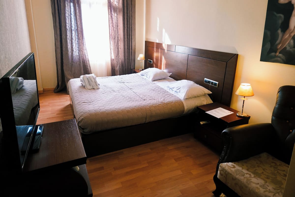A hotel room with a bed, a desk, a chair, a lamp, and a painting on the wall.