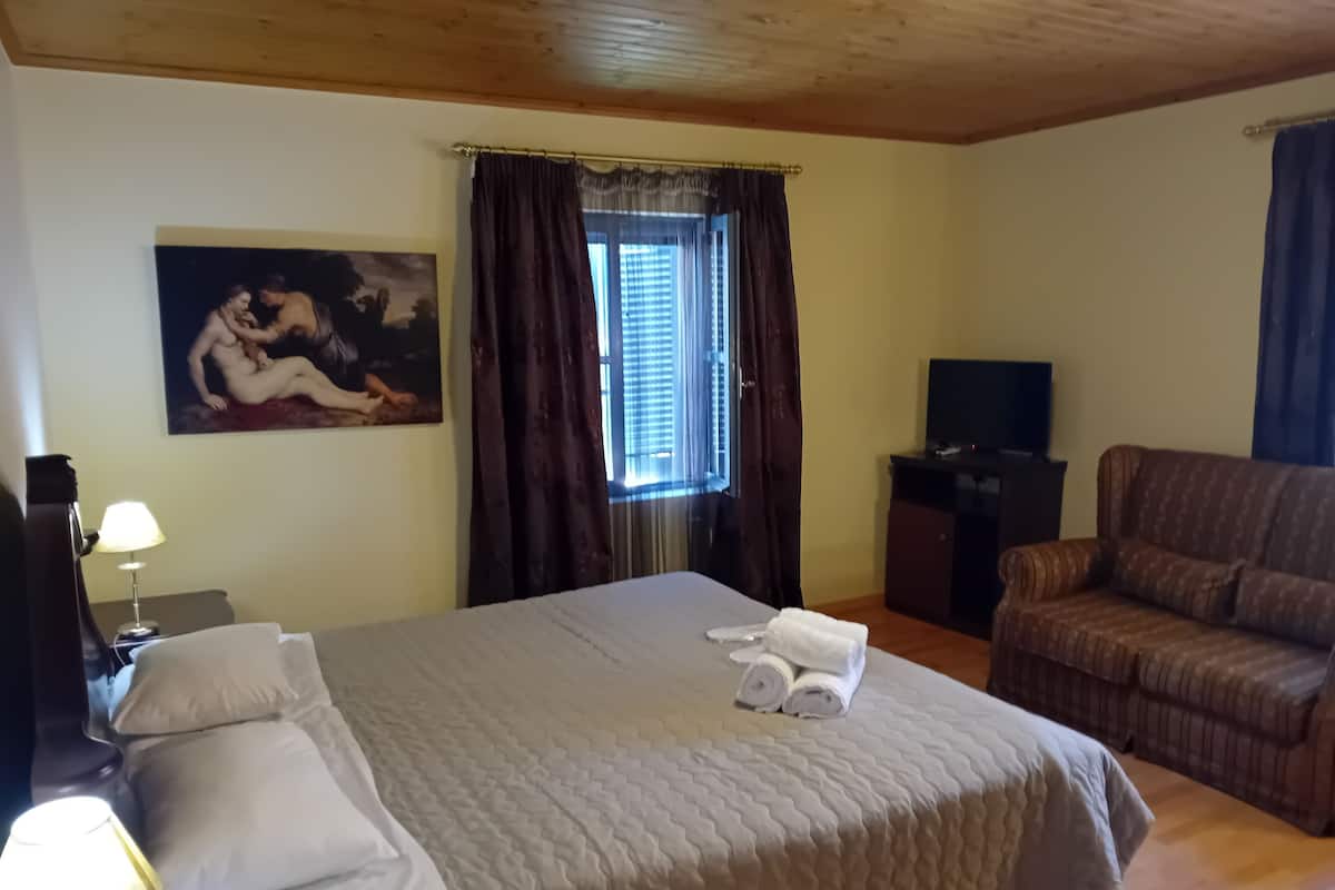 A hotel room with a large bed, a TV, a sofa, and a painting on the wall.